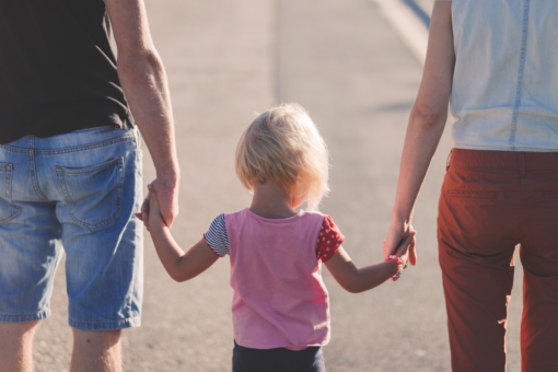 Young child facing away from camera, holding hands with two adults out of shot.