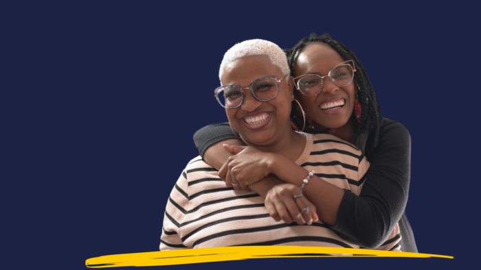 Two smiling women cuddling, against a navy background.