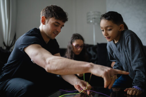 Tom Daley playing a game with a small boy in a living room.