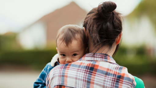 A woman facing away from the camera with a young child looking at the camera over her shoulder.