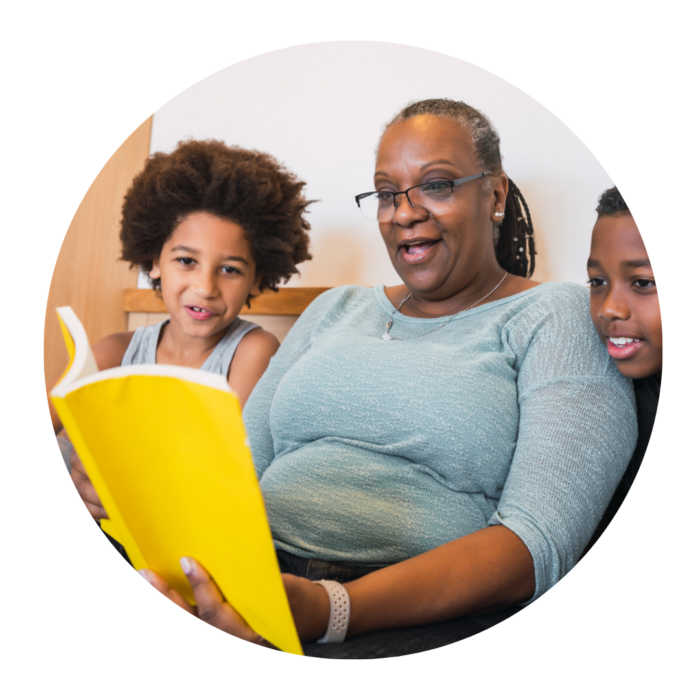 An older woman reads from a yellow book, with a young boy on either side of her.