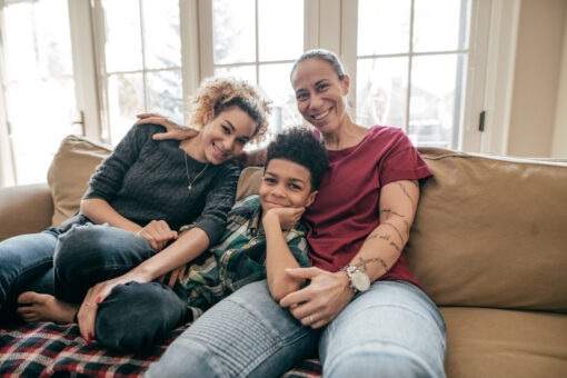 An adult, a teenager and a young boy sitting on a sofa, smiling.