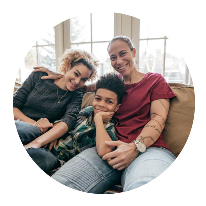 An adult, a teenager and a young boy sitting on a sofa, smiling.