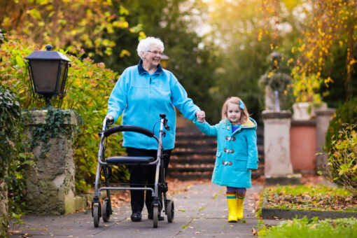 An older woman with a walking aid walks hand-in-hand with a small girl in wellington boots.