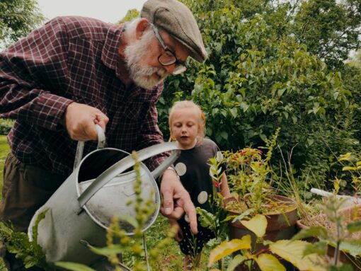 a small child is watching as an older man waters a plant in the garden.