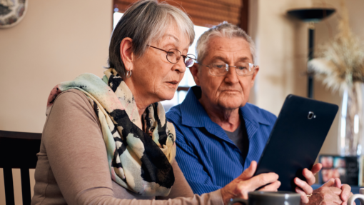 Older couple sitting at the kitchen table looking at a tablet computer.