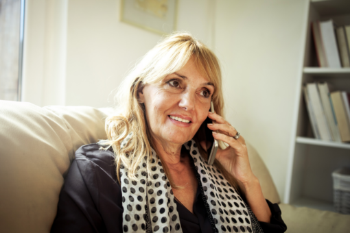 A woman sitting on the sofa with her ear to a mobile phone. She has a neutral expression.