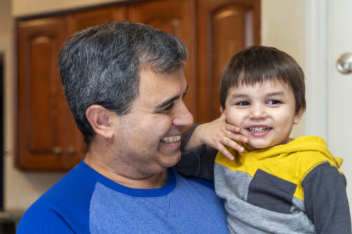 Close-up of a man holding a small boy against his shoulder. They are both smiling.