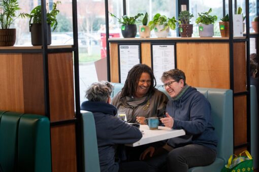 Three adults sitting in a booth at a cafe, sharing a drink and laughing.