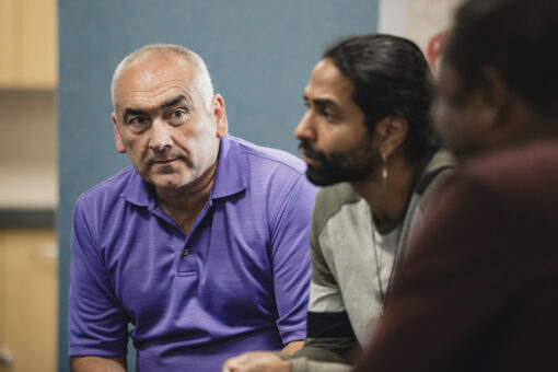 Close-up of three men sitting in a semi-circle listening to someone talking.