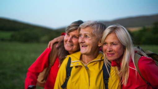 Three women in hiking gear huddling together to look at something off-screen in the countryside.