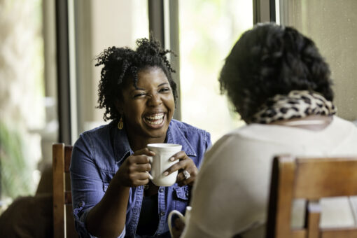 Two women, laughing and chatting over a hot drink.