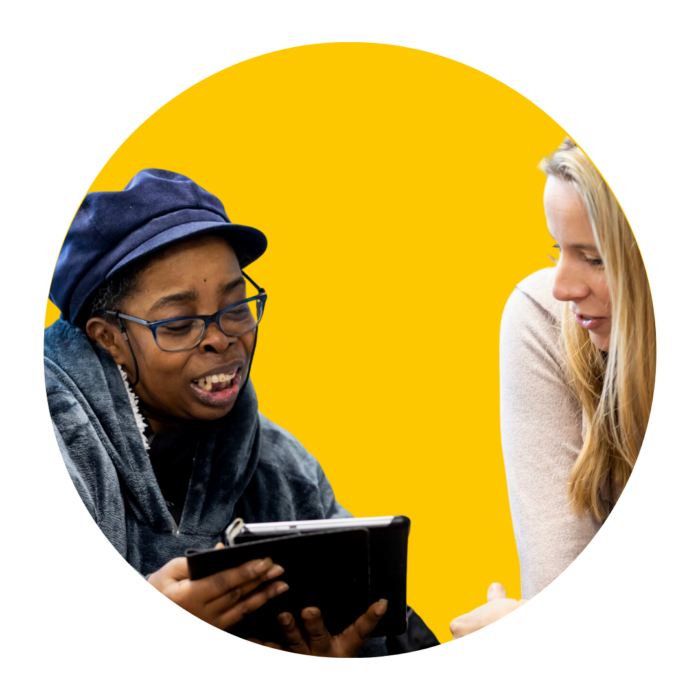 Two women looking at a tablet against a yellow background.