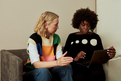 Two women sitting side by side on a sofa looking at a laptop screen.