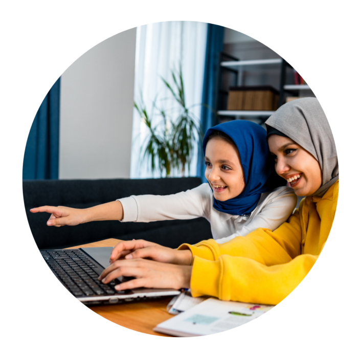 A woman and little girl, both wearing headscarves, look at a laptop. They are both smiling.