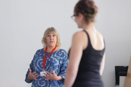 Two women standing in an empty room. One of them is wearing a lanyard and gesturing.