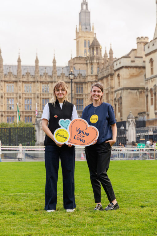 Two women standing in front of the Houses of Parliament, holding a sign that says 