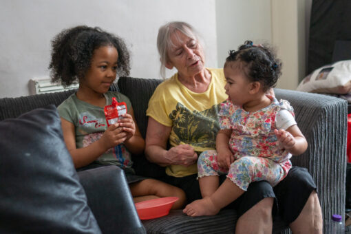 An older woman sits with two small children on the sofa.