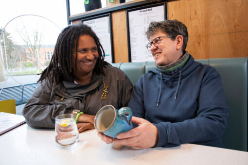 Two people chatting in a cafe booth. They are both smiling.