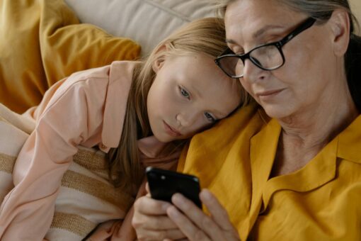 An older woman and a small child watching something on a mobile phone. The child is leaning her head on the older woman's shoulder.