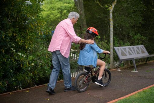 An older man is supporting a child riding a bicycle in the park.